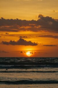the sun is setting over the ocean on a cloudy day